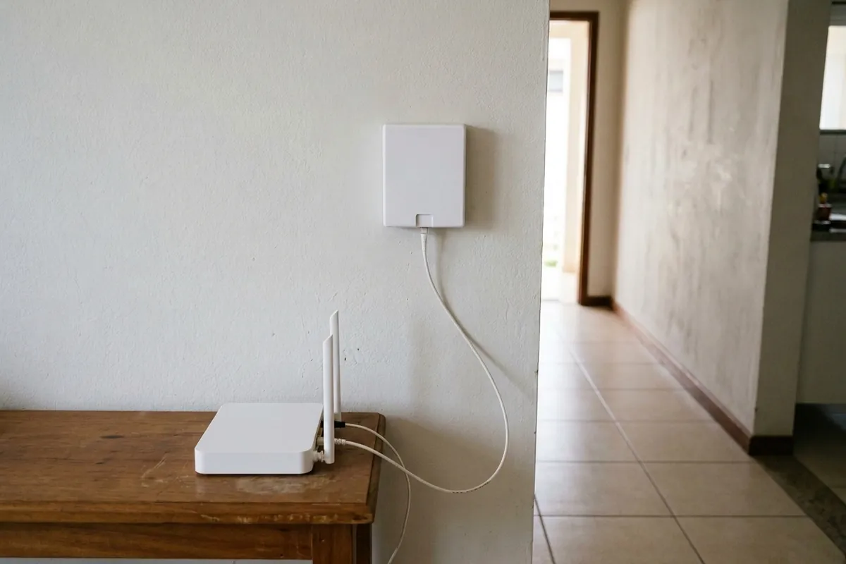 Cabo de fibra saindo da caixinha de terminação óptica na parede até o roteador